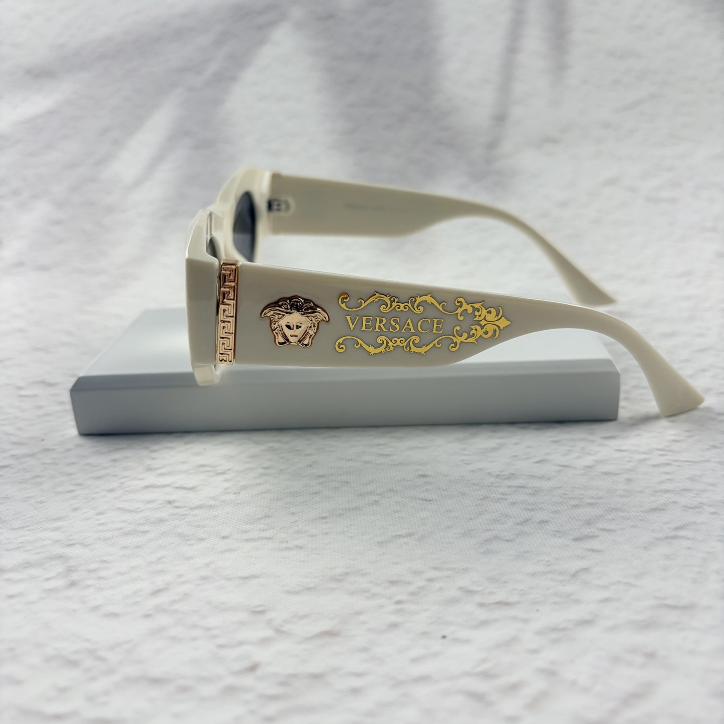 Off-white geometric cat-eye sunglasses with gold metal side accents, resting on a white stand.