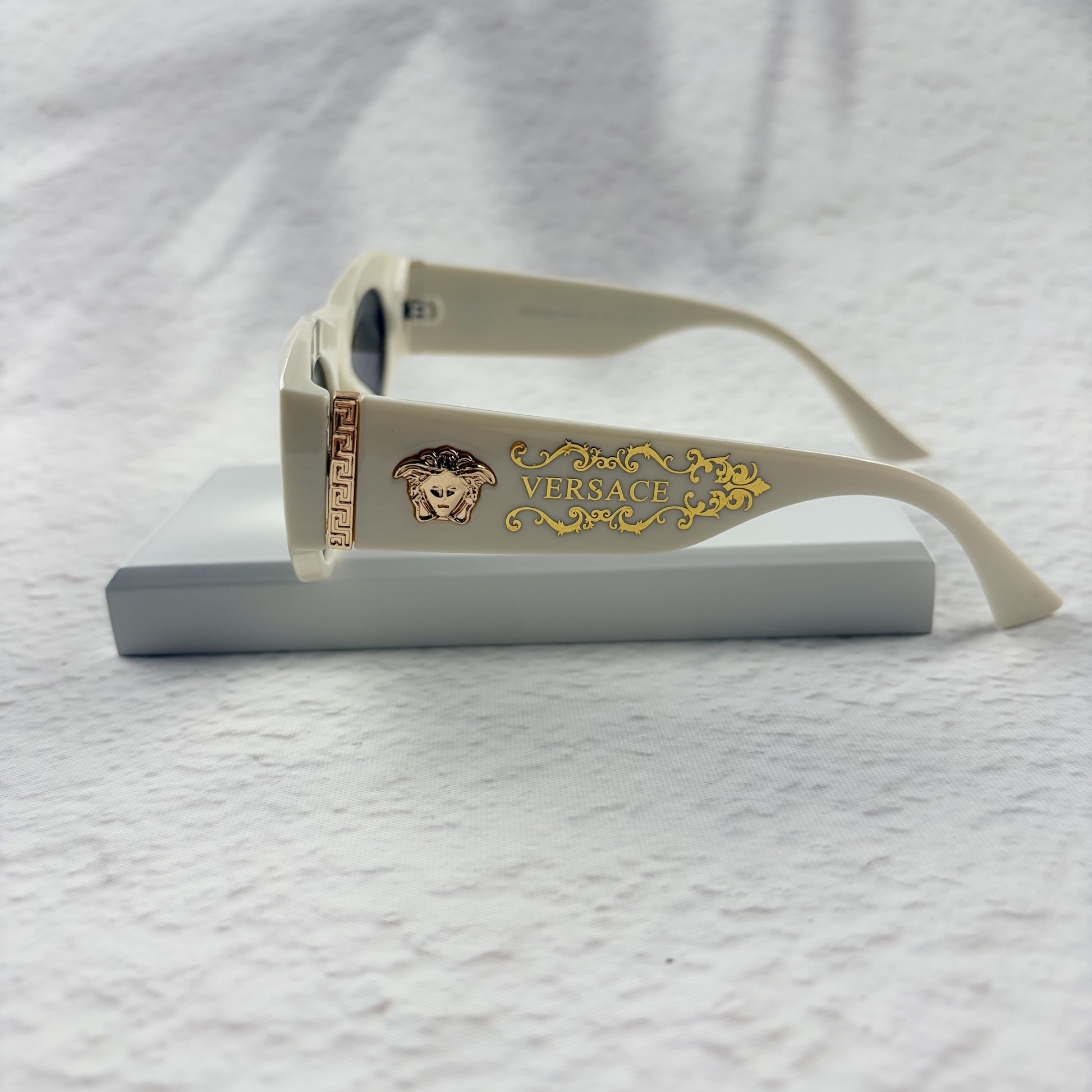 Off-white geometric cat-eye sunglasses with gold metal side accents, resting on a white stand.