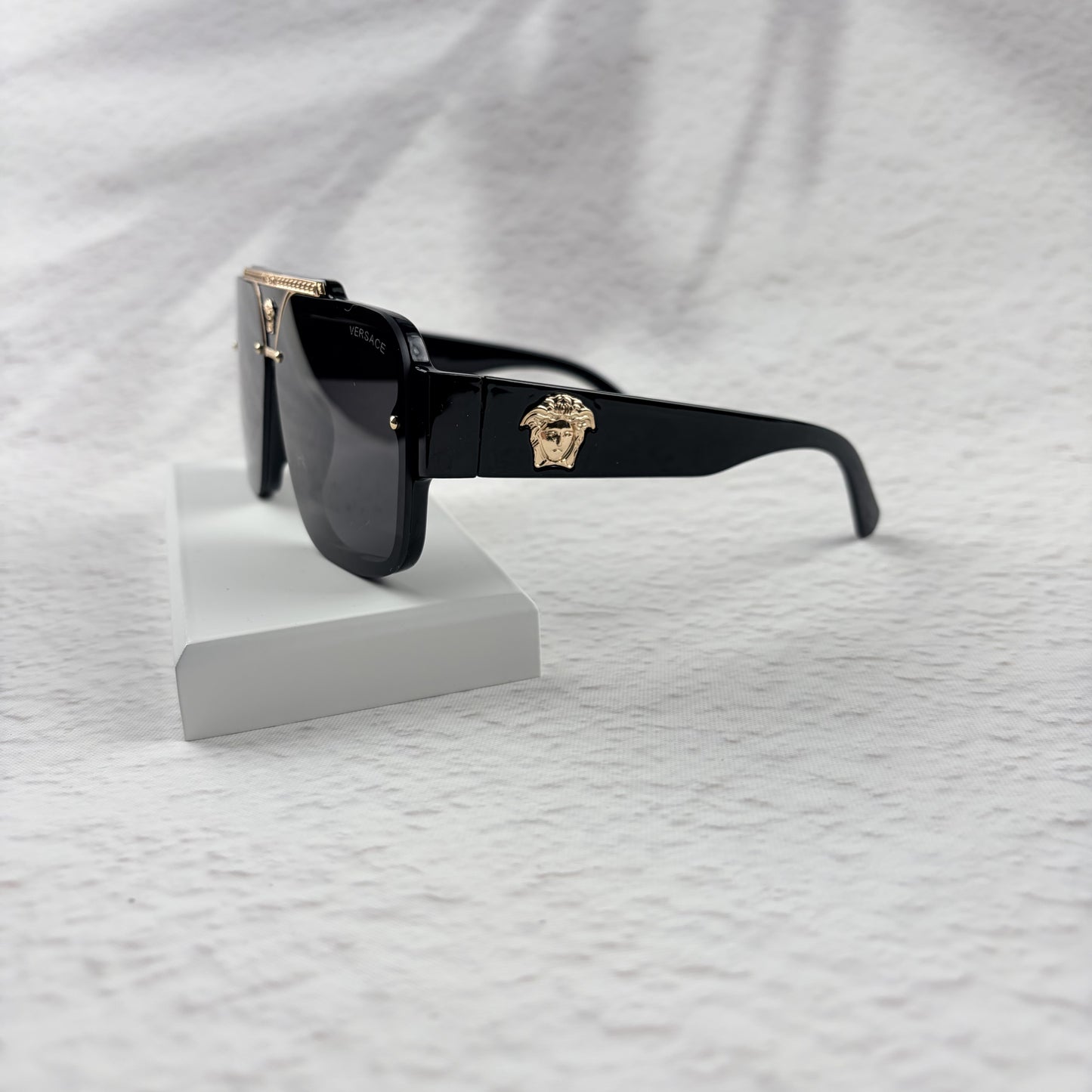 Oversized black flat-top sunglasses with a gold metal bridge and gold emblems on the temples.