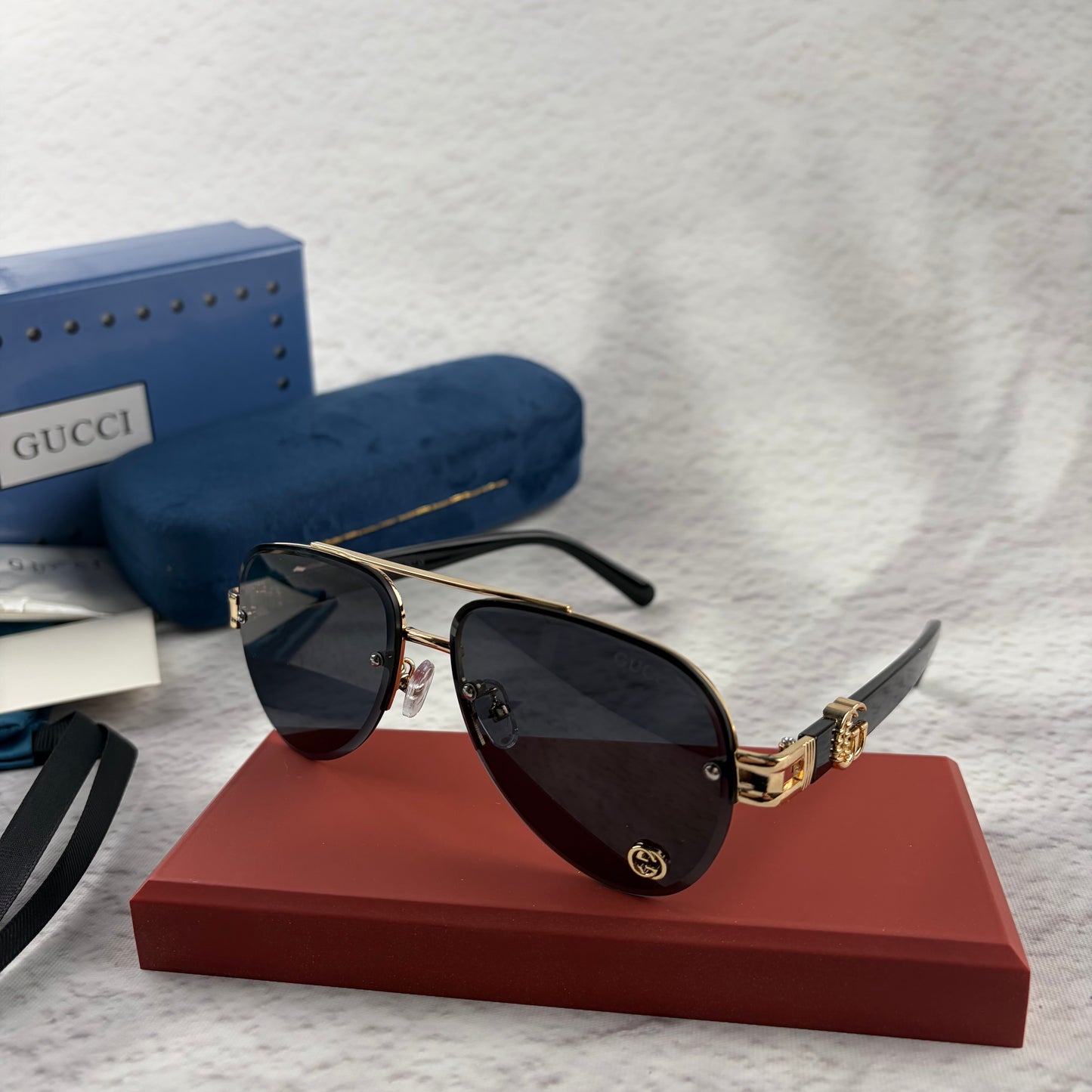 Pilot sunglasses with gold frame accents and dark lenses on a red display case.