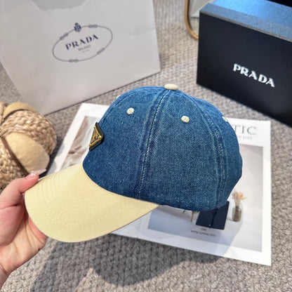 A two-tone baseball cap with a blue denim crown, beige brim, and a triangular metal logo badge.