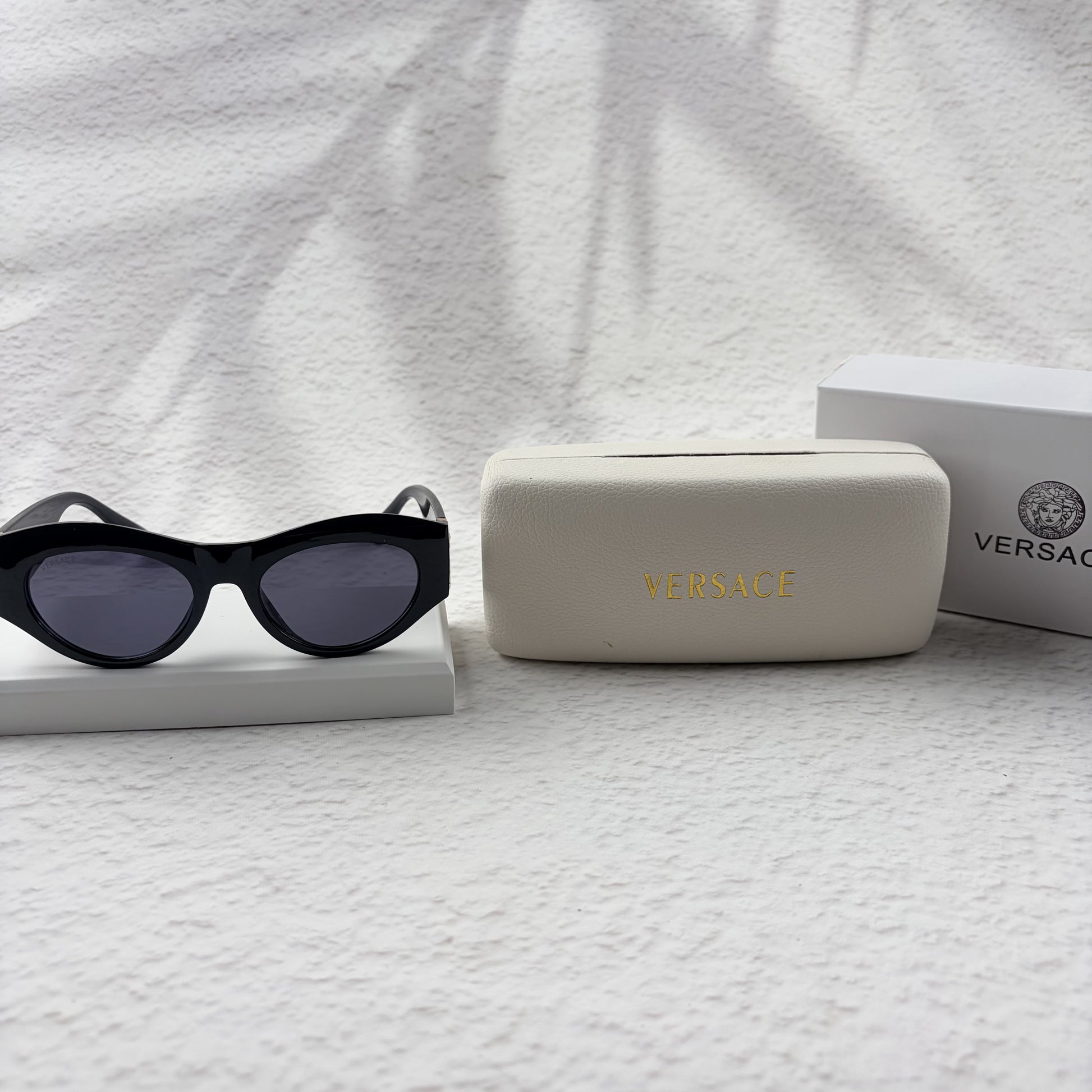 Black cat-eye sunglasses featuring gold-toned baroque temple embellishments on a white textured base