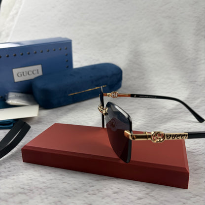 Rimless rectangular sunglasses with gold-tone metal arms and dark lenses on a red display stand.
