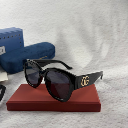 Oversized black frame sunglasses with dark gradient lenses and gold-tone logo detailing on temples.