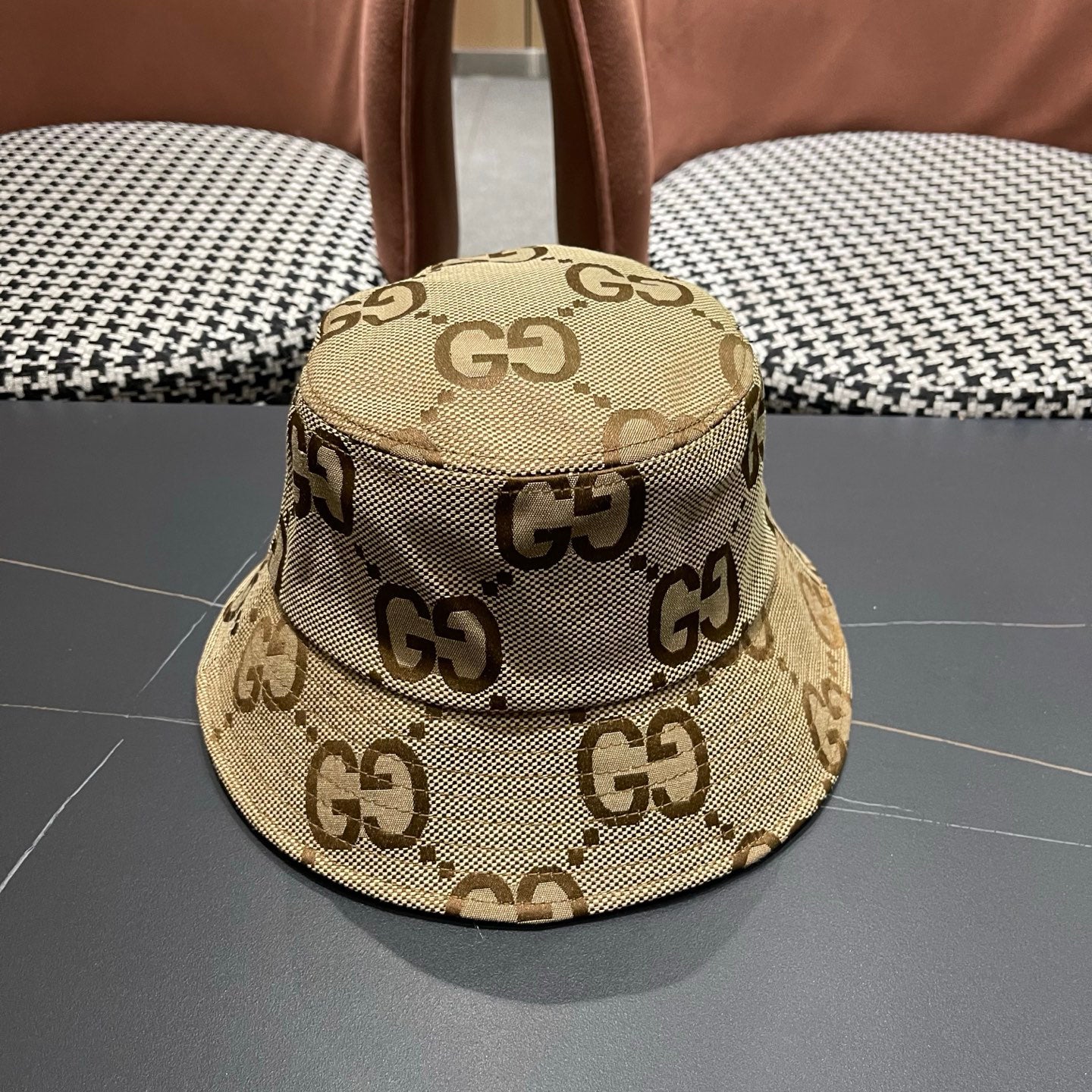 A beige canvas bucket hat with an all-over brown monogram pattern and a decorative gold-toned emblem
