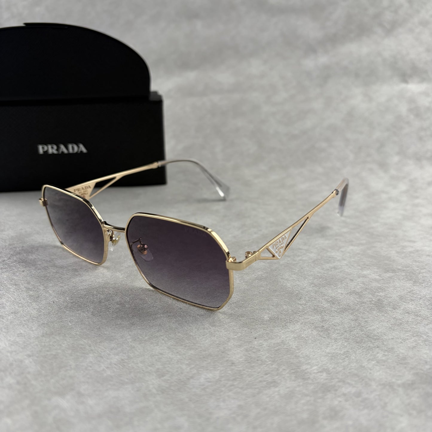 A pair of gold-toned geometric frame sunglasses with gradient lenses, displayed with a black protect