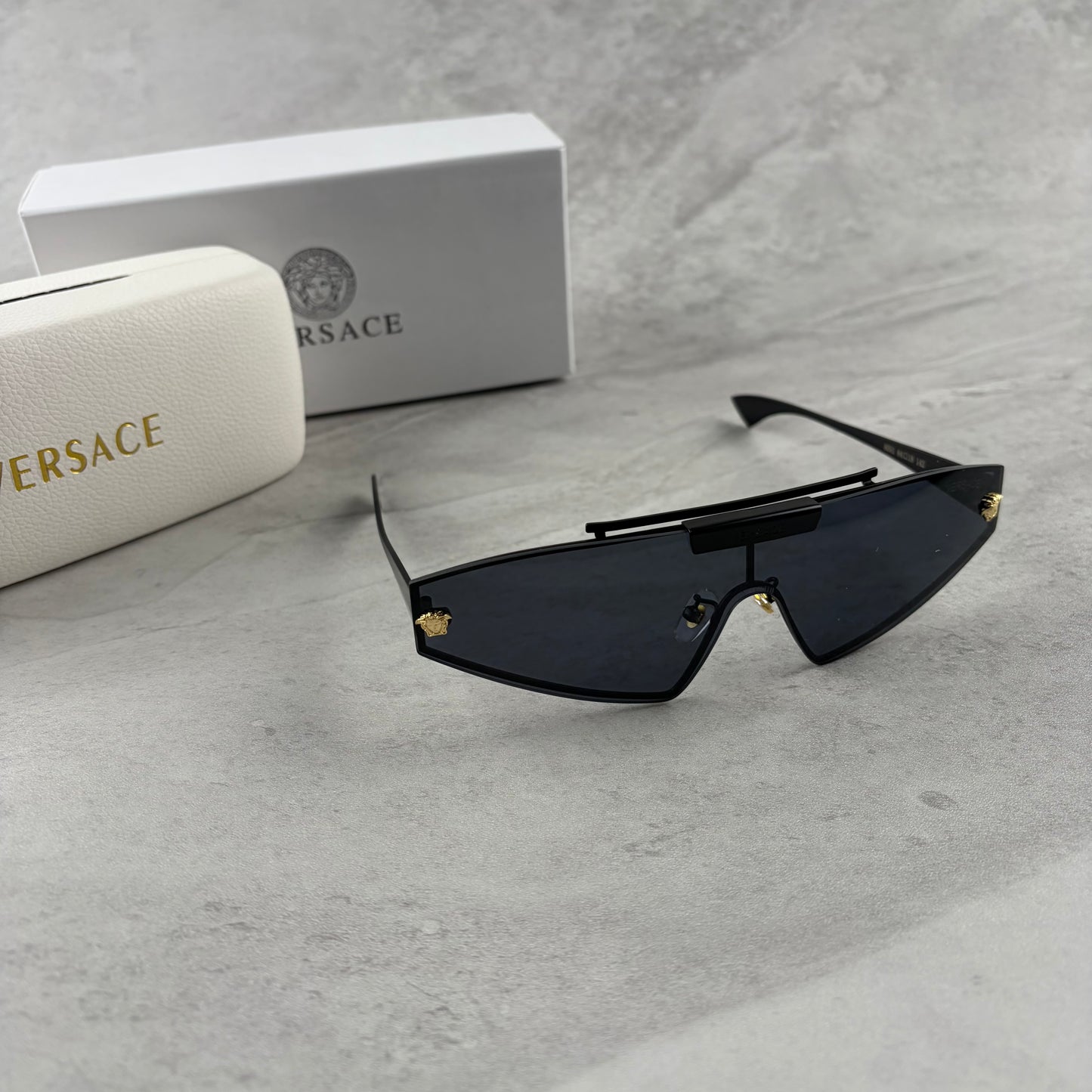 Modern shield sunglasses with a sleek black frame and dark tinted lenses on a grey background.