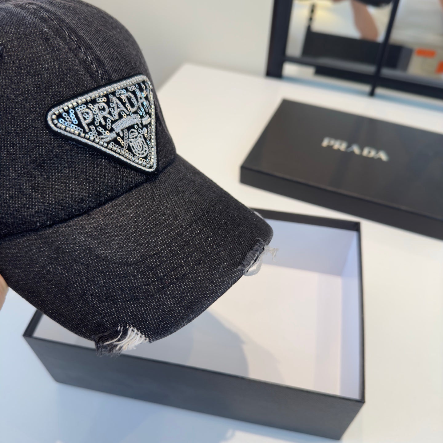 A black distressed denim baseball cap with a sparkling triangular patch on the front center.
