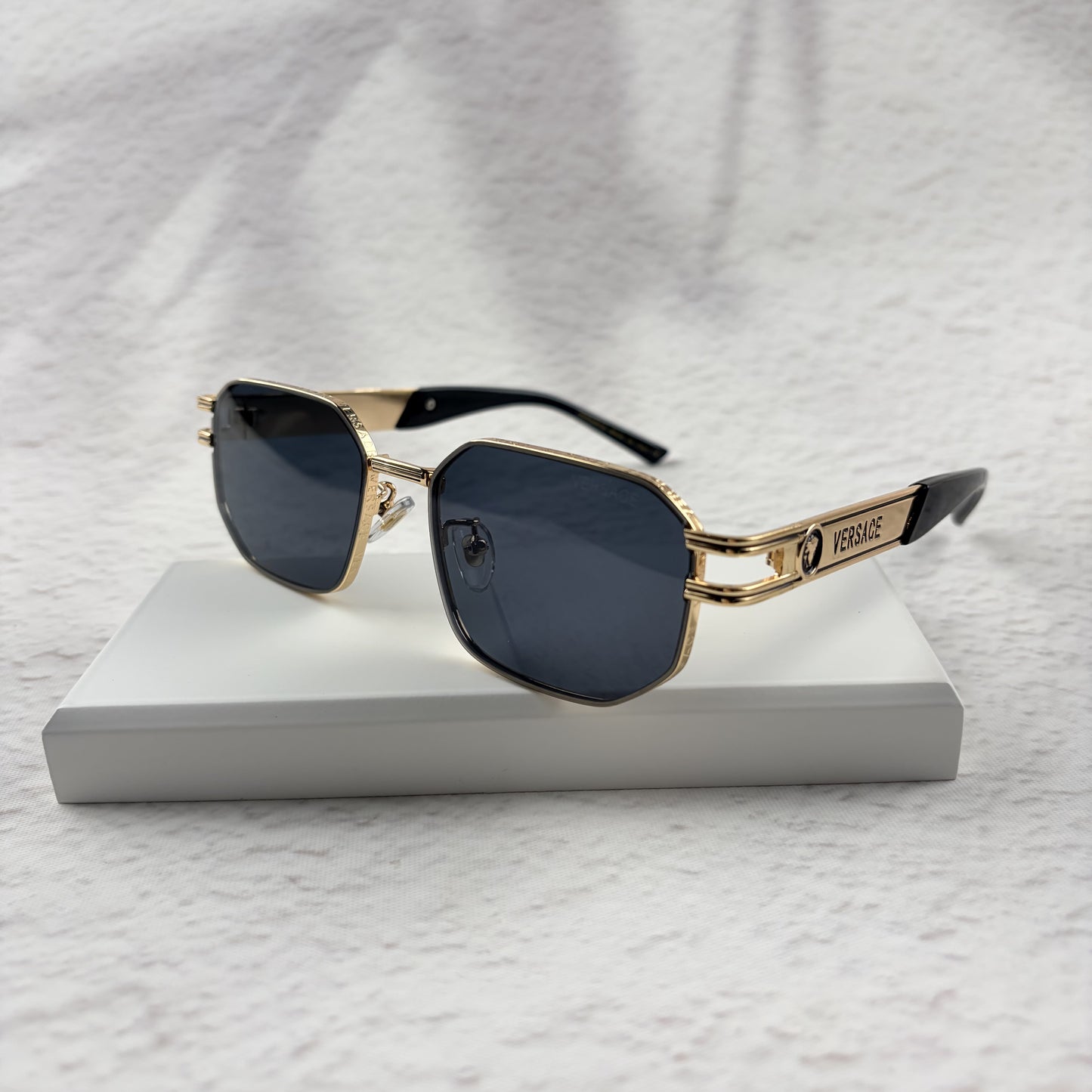 Gold tone metal frame geometric sunglasses with dark lenses on a white display block.