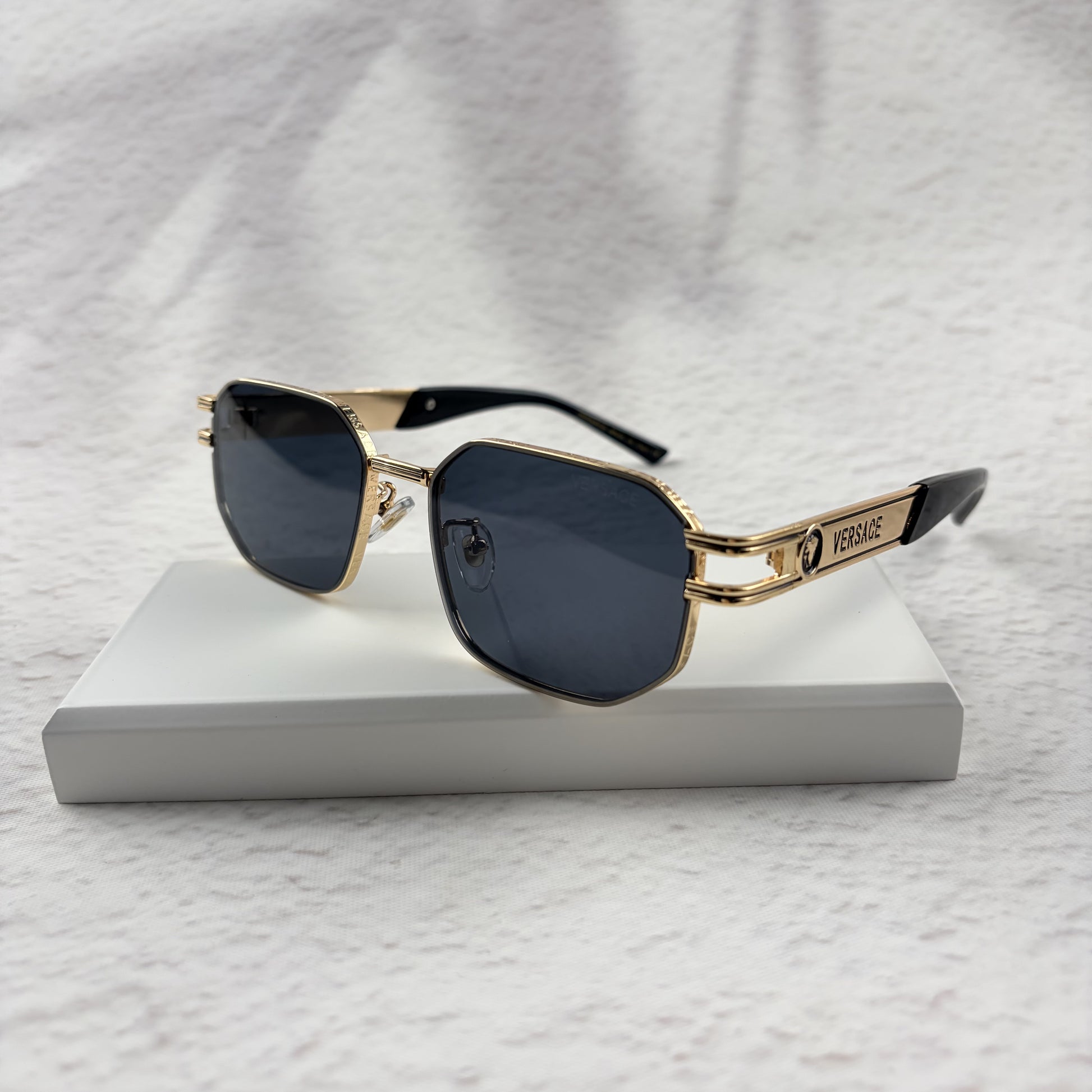 Gold tone metal frame geometric sunglasses with dark lenses on a white display block.
