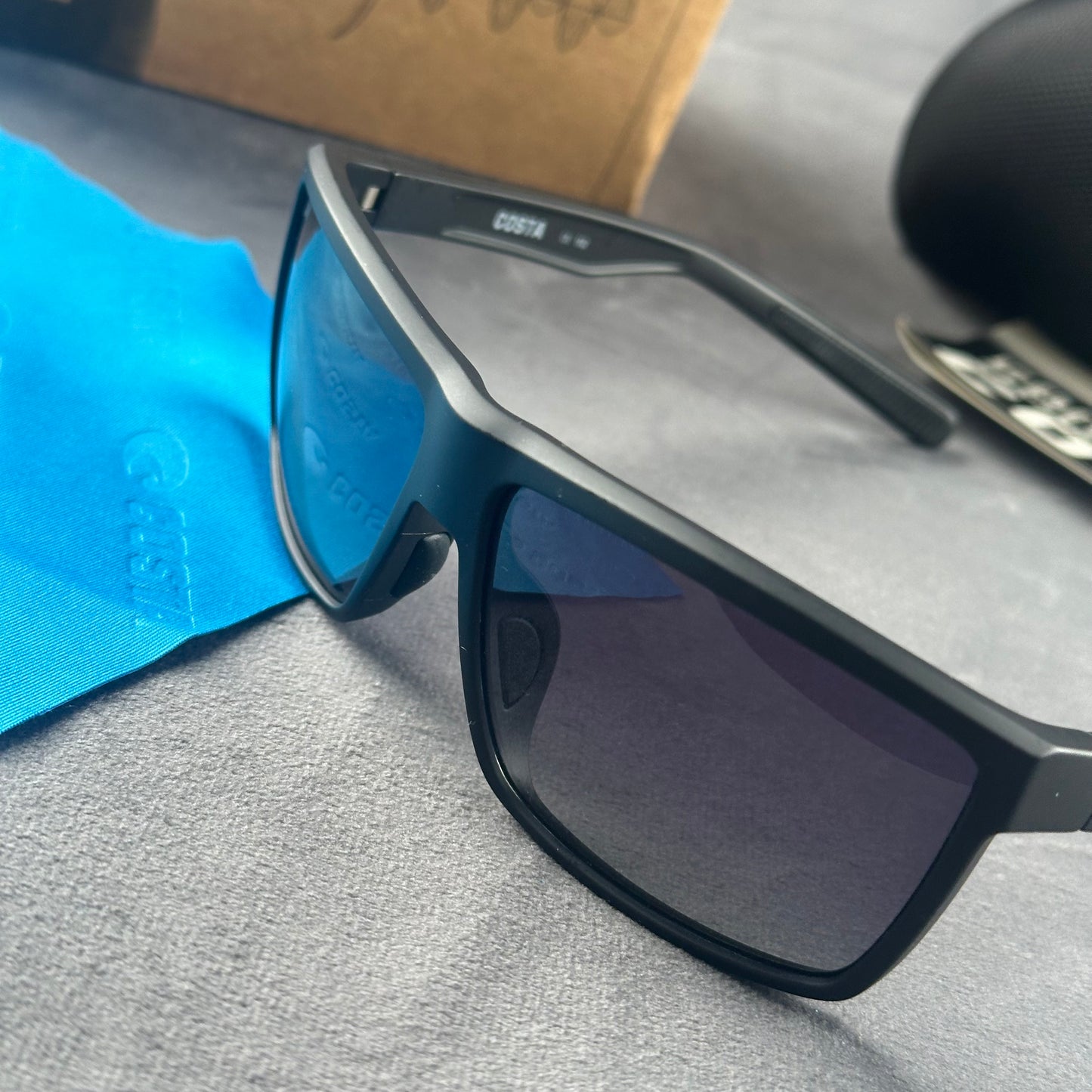 Matte black sport sunglasses with polarized blue-tinted lenses, hard case, and cleaning cloth.