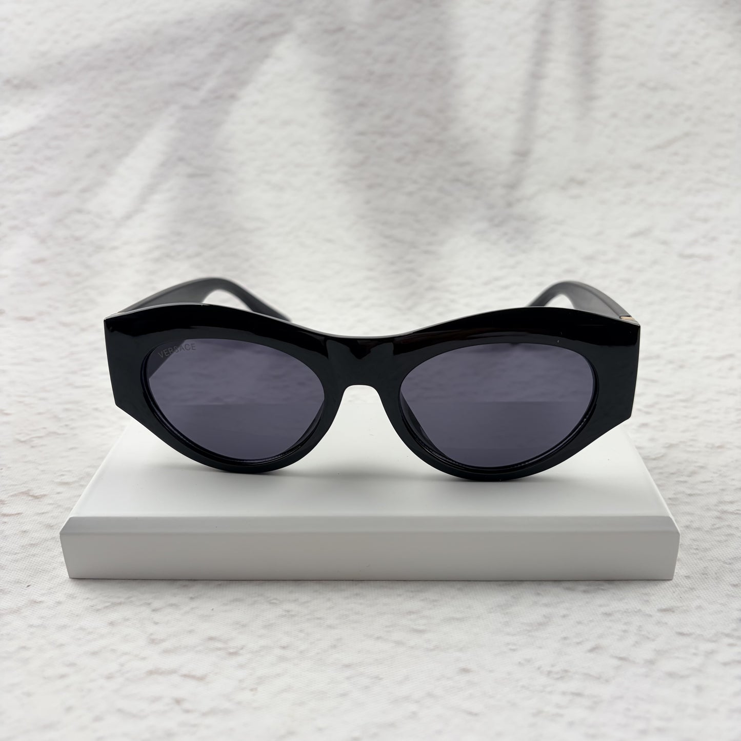 Black cat-eye sunglasses featuring gold-toned baroque temple embellishments on a white textured base