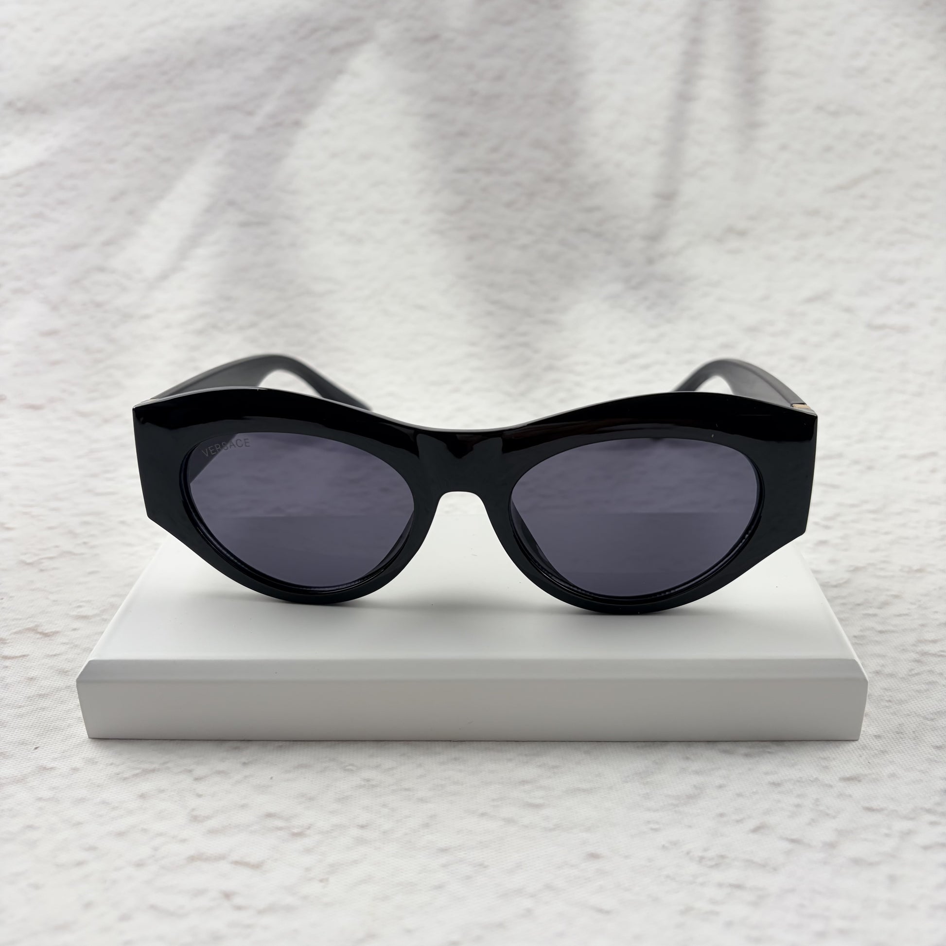 Black cat-eye sunglasses featuring gold-toned baroque temple embellishments on a white textured base