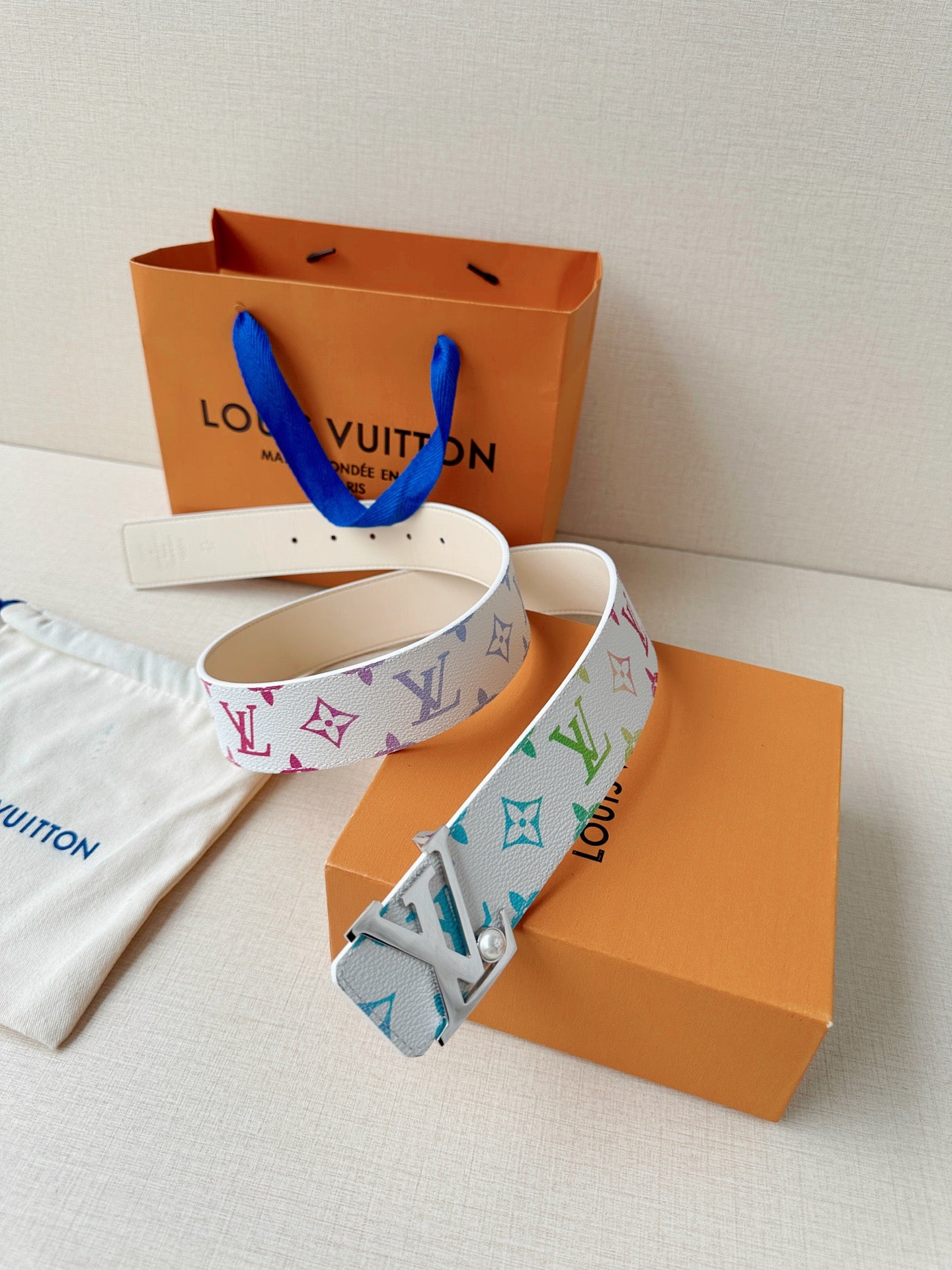 A white leather belt with colorful monogram print and a silver buckle with a pearl accent.