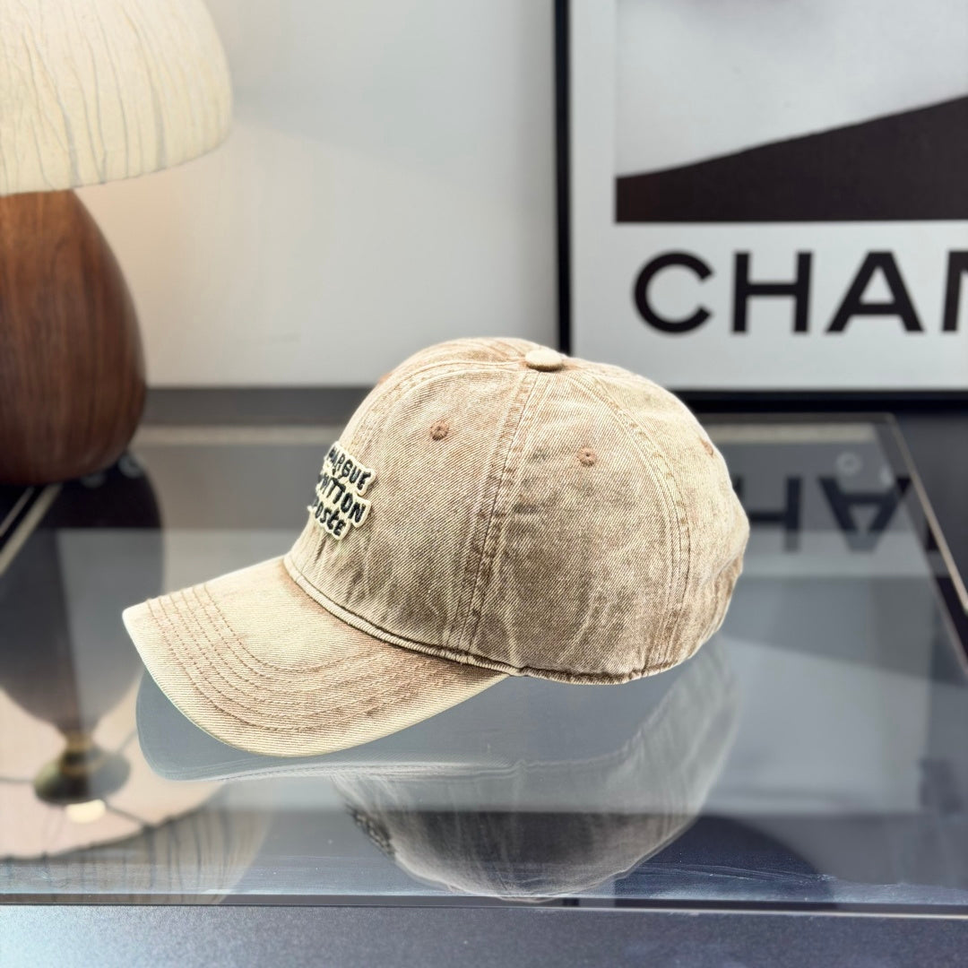 Vintage style distressed light brown denim baseball cap with embroidered letter patch on front.