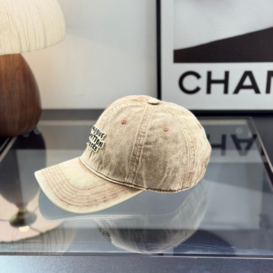 Vintage style distressed light brown denim baseball cap with embroidered letter patch on front.