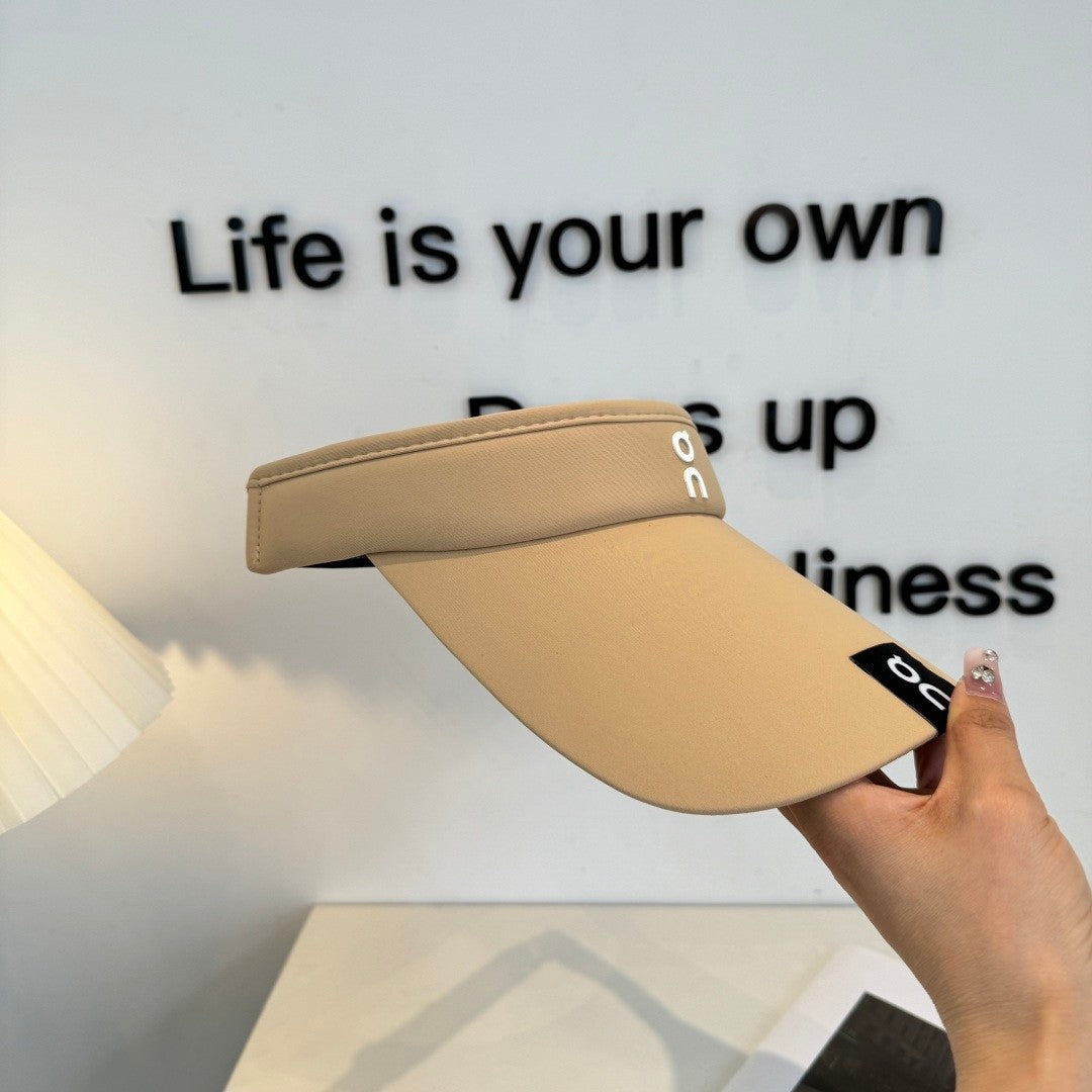 A beige lightweight sport visor with adjustable elastic band, featuring a minimalist logo design.