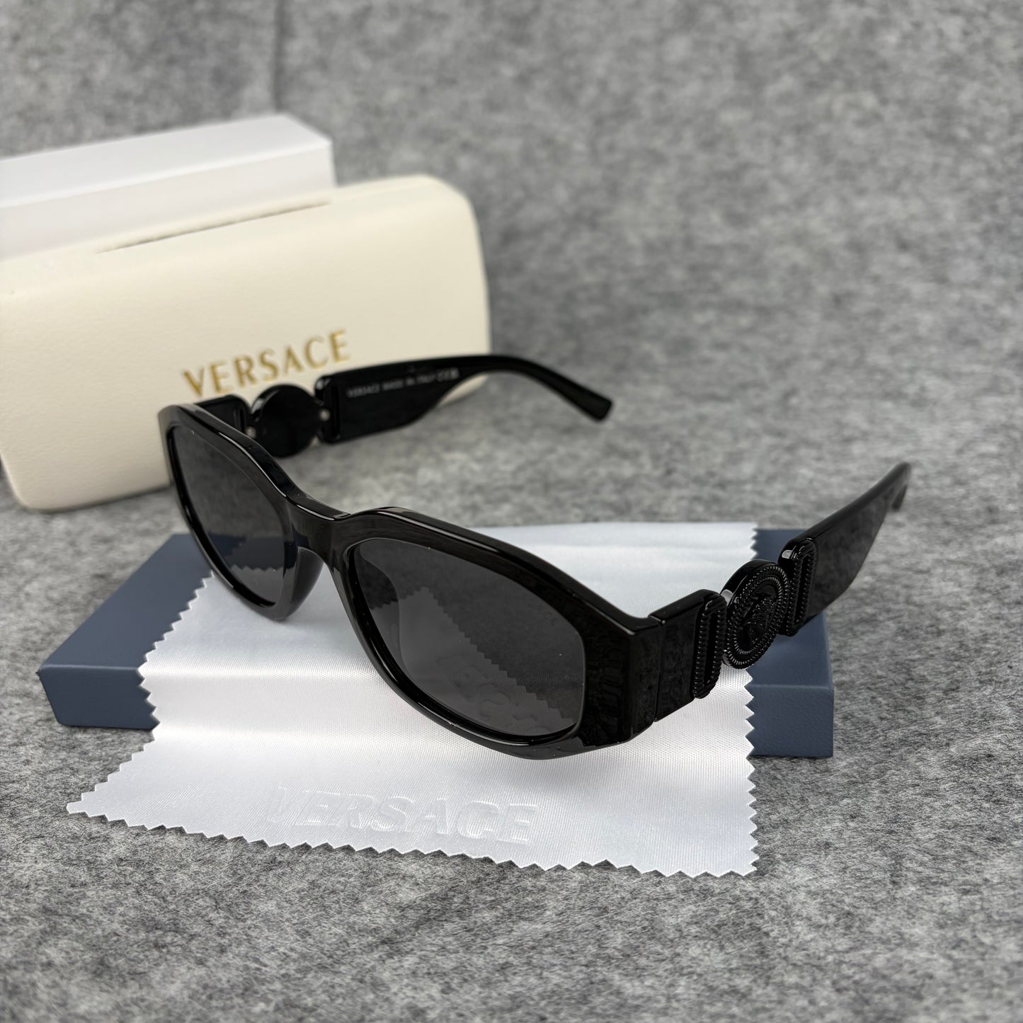 A pair of sleek black oval sunglasses resting on a cleaning cloth next to a white protective case.