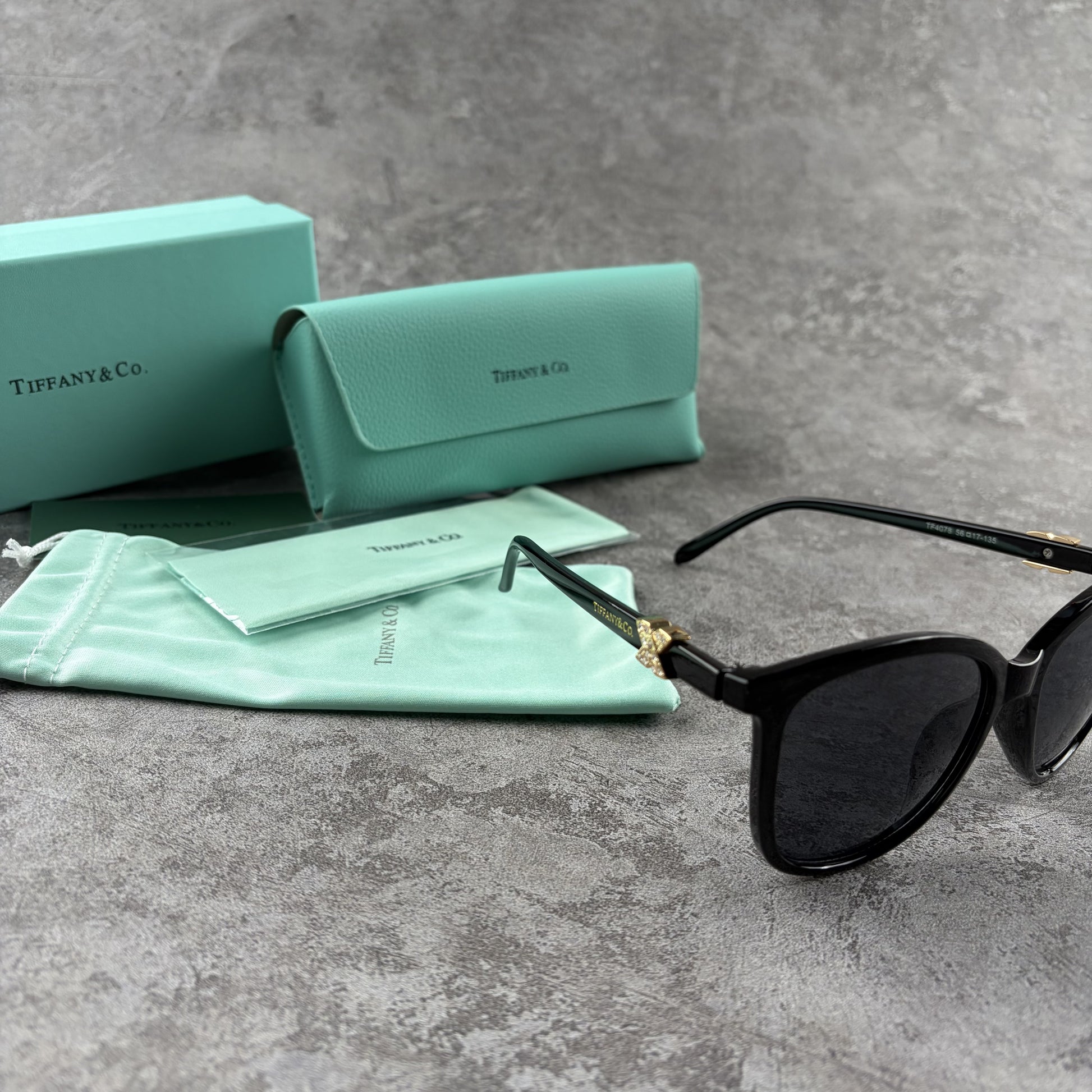 Black cat-eye sunglasses with decorative side temple accents, presented with a branded protective ca