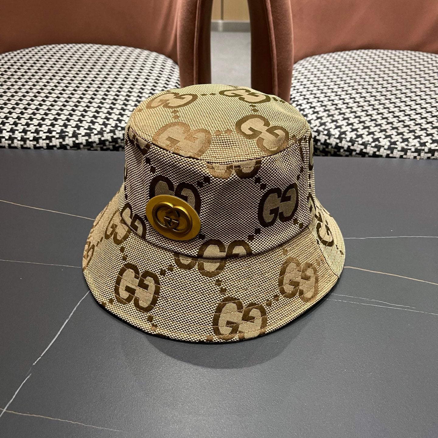 A beige canvas bucket hat with an all-over brown monogram pattern and a decorative gold-toned emblem
