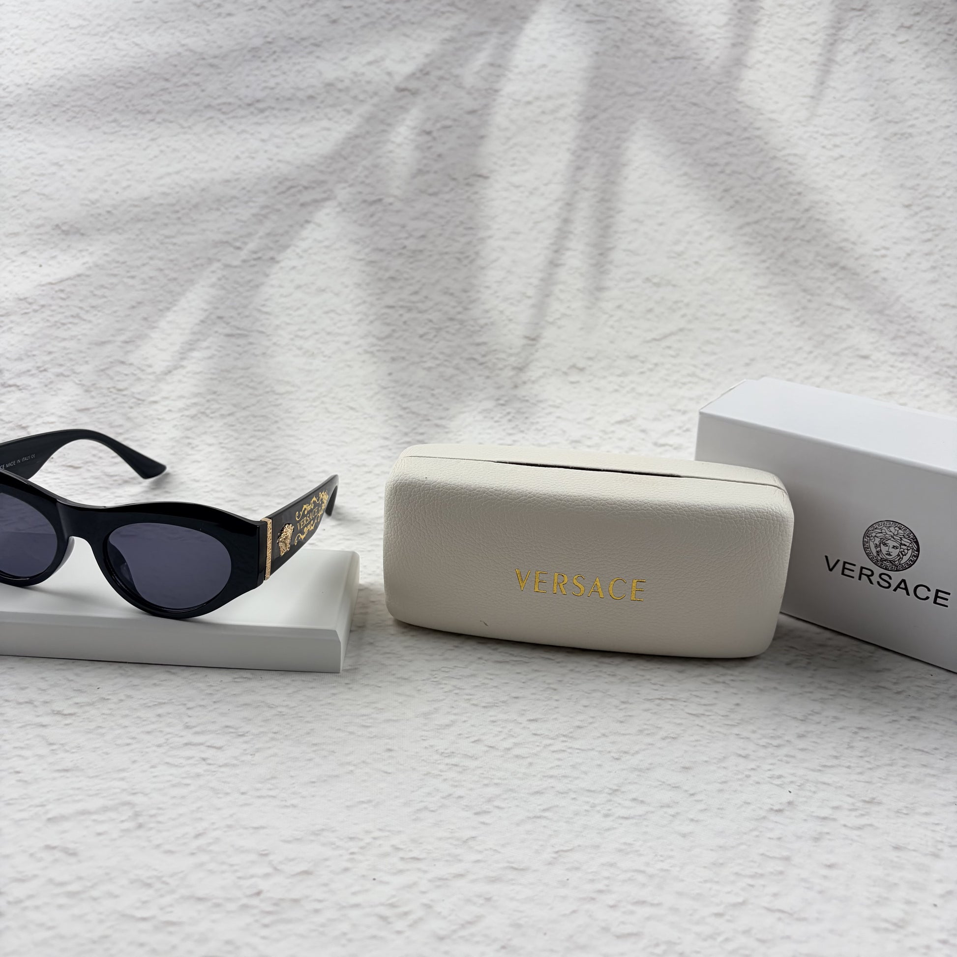 Black cat-eye sunglasses featuring gold-toned baroque temple embellishments on a white textured base