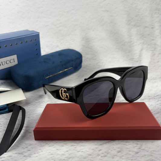 Oversized black frame sunglasses with dark gradient lenses and gold-tone logo detailing on temples.