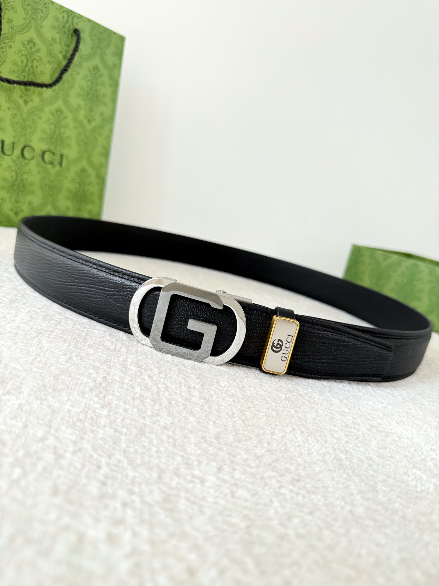 Black textured genuine leather belt with a modern metallic geometric buckle on a white surface.