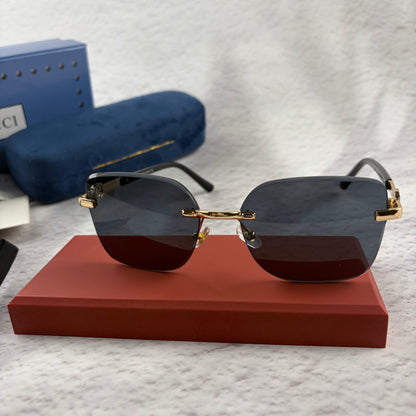 Rimless rectangular sunglasses with gold-tone metal arms and dark lenses on a red display stand.