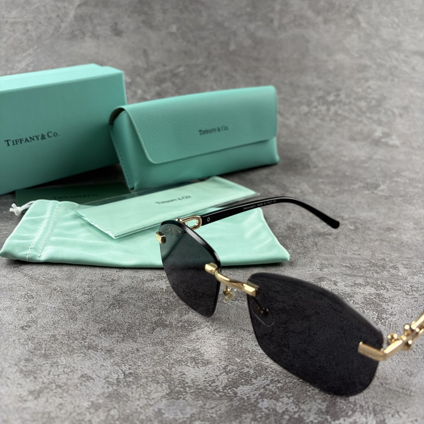 Rimless gradient sunglasses with gold-tone metal frames and black temple arms on a grey surface.