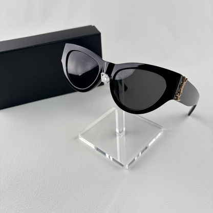 A pair of black cat-eye sunglasses with gold-tone hardware on the temples, displayed on a stand.