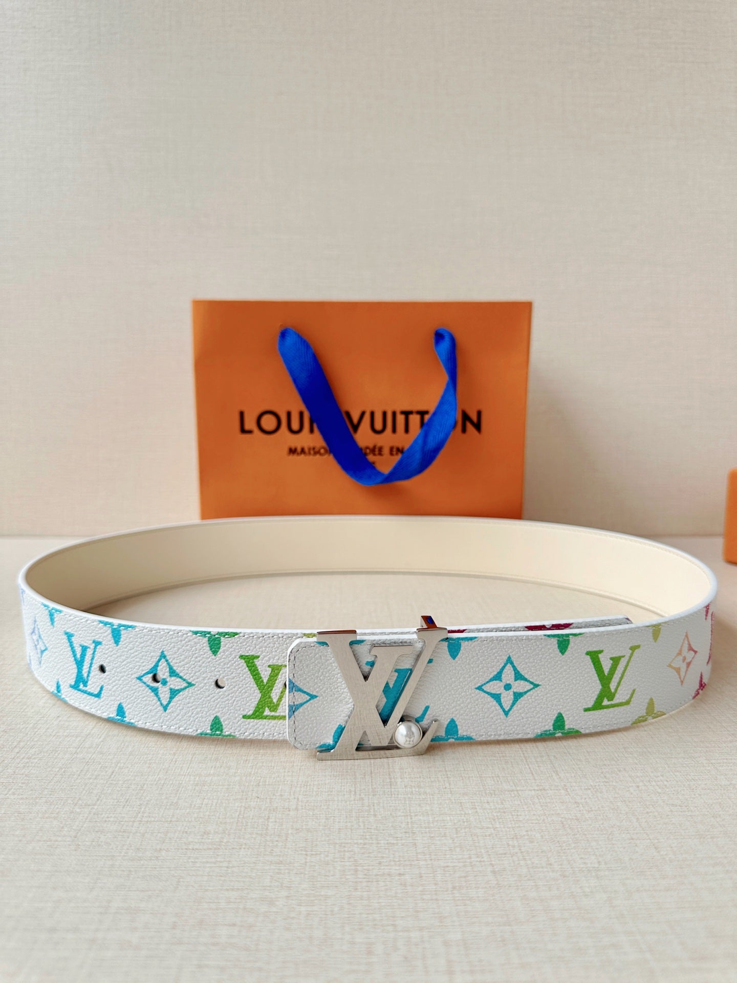 A white leather belt with colorful monogram print and a silver buckle with a pearl accent.