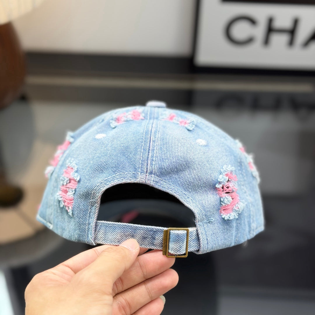 Distressed light wash denim baseball cap with frayed pink stitching and embroidery on the front.