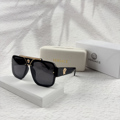 Oversized black flat-top sunglasses with a gold metal bridge and gold emblems on the temples.