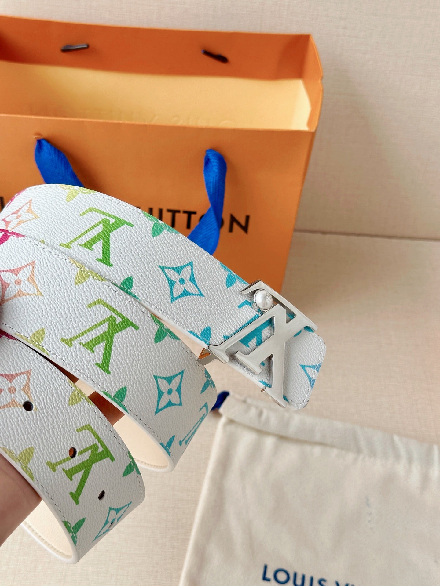 A white leather belt with colorful monogram print and a silver buckle with a pearl accent.