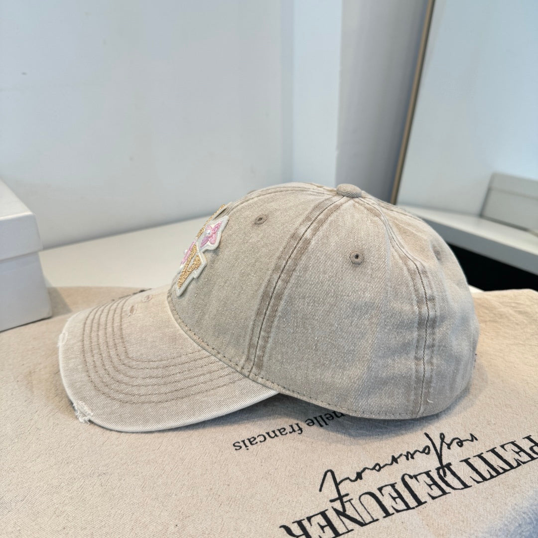 Distressed beige baseball cap with intricate floral letter embroidery and pearl details.