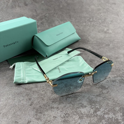Rimless sunglasses with gradient blue lenses and gold-tone metal arms, displayed with protective cas