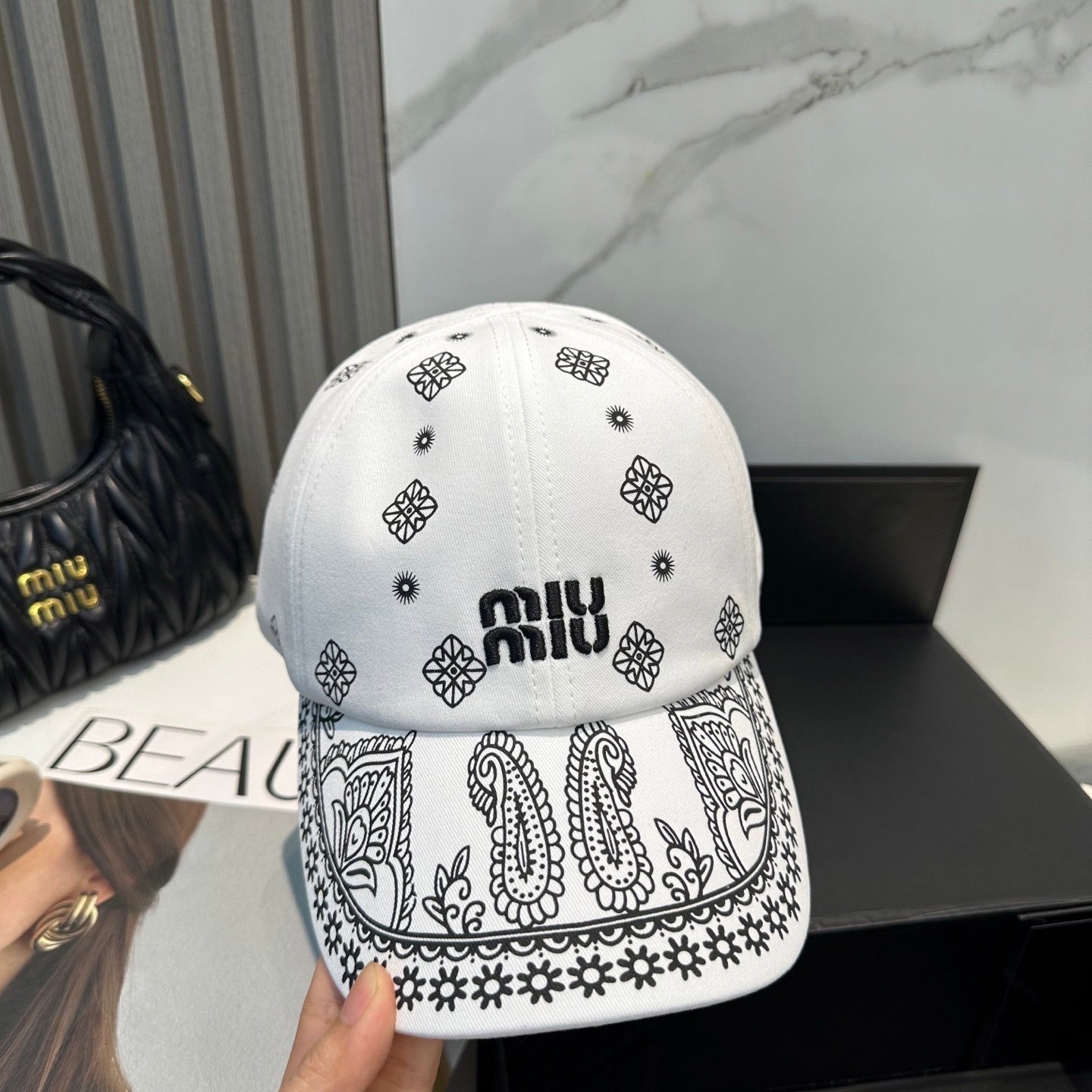White cotton baseball cap with black paisley patterns and an adjustable drawstring back closure.