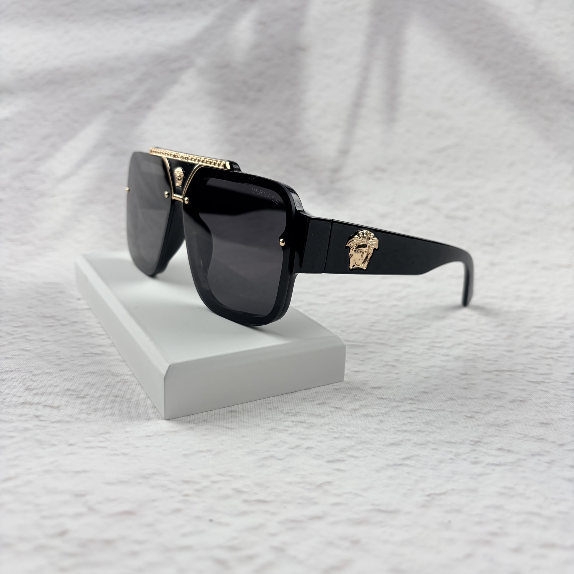Oversized black flat-top sunglasses with a gold metal bridge and gold emblems on the temples.
