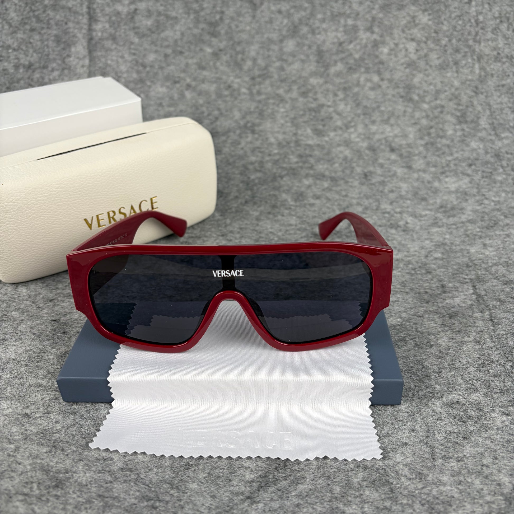 Oversized bold red shield sunglasses with dark lenses on a grey background with a white case.