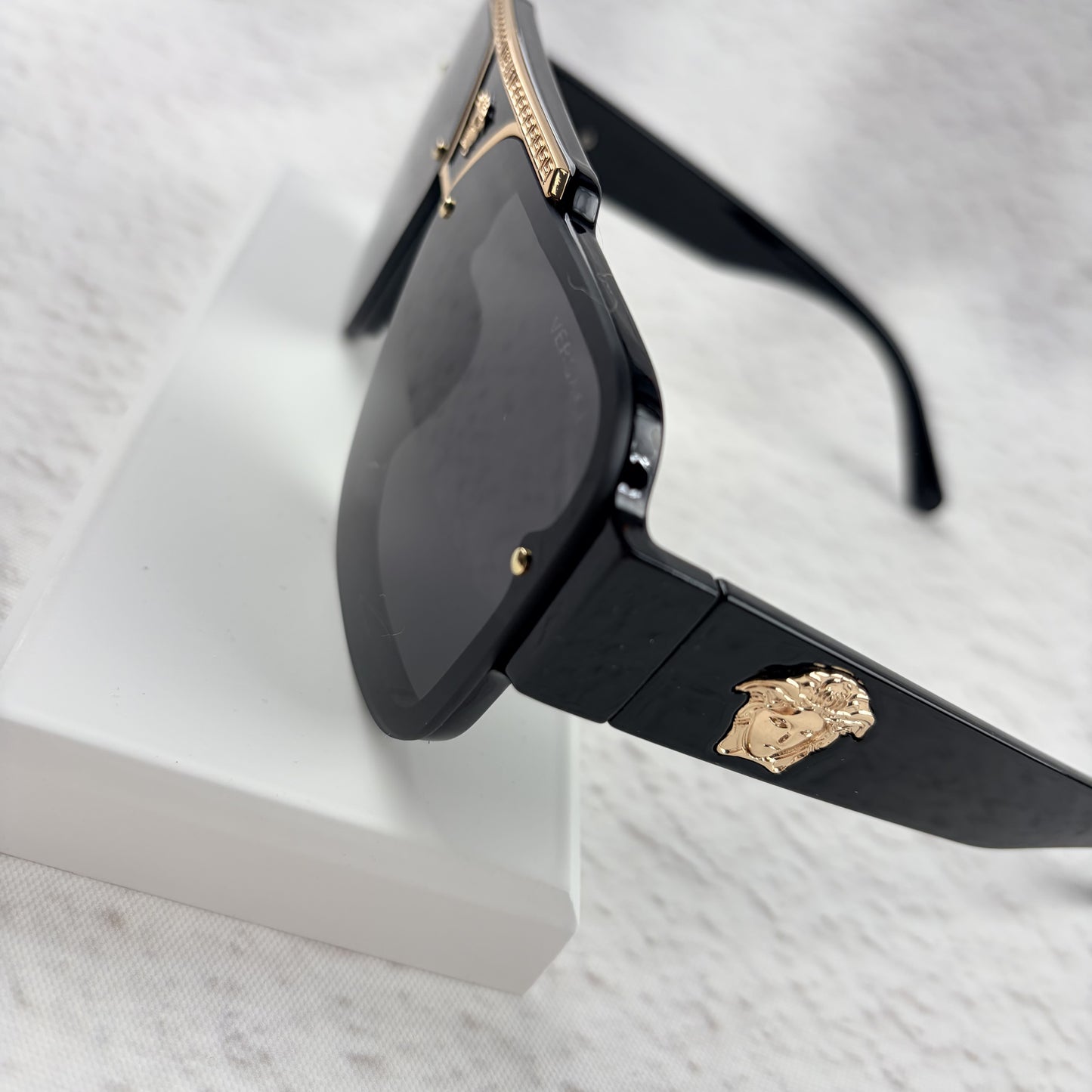 Oversized black flat-top sunglasses with a gold metal bridge and gold emblems on the temples.