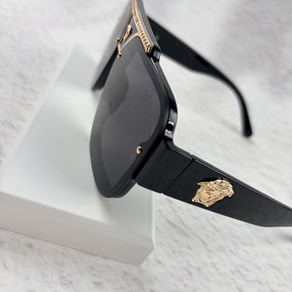 Oversized black flat-top sunglasses with a gold metal bridge and gold emblems on the temples.