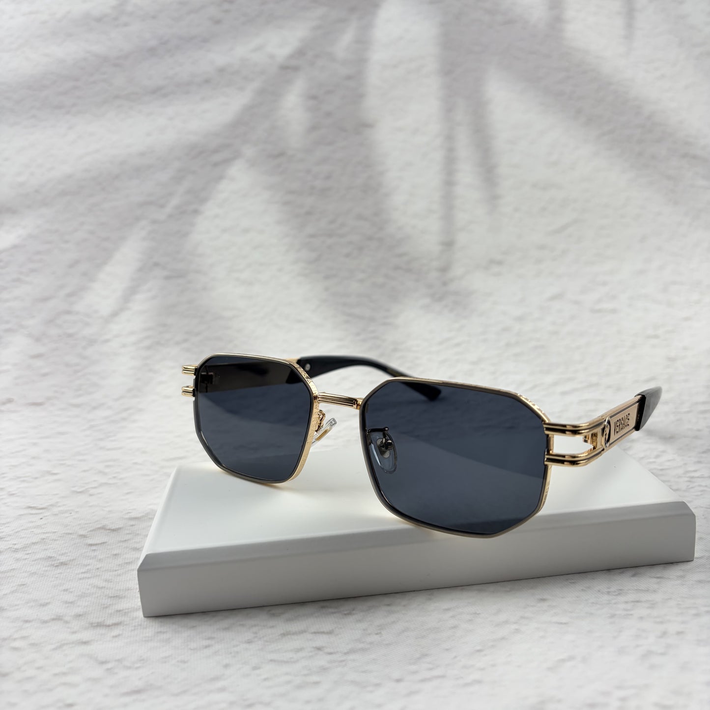 Gold tone metal frame geometric sunglasses with dark lenses on a white display block.
