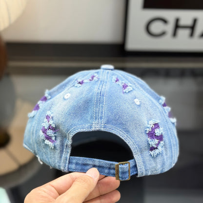 Distressed blue denim baseball cap with frayed detailing and a central stitched logo emblem.