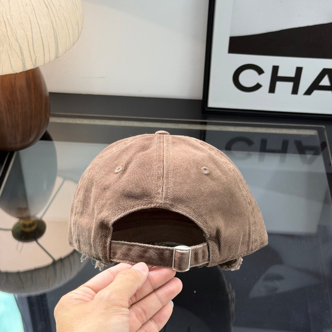 Distressed brown cotton baseball cap with frayed brim and minimalist metal circular side detail.