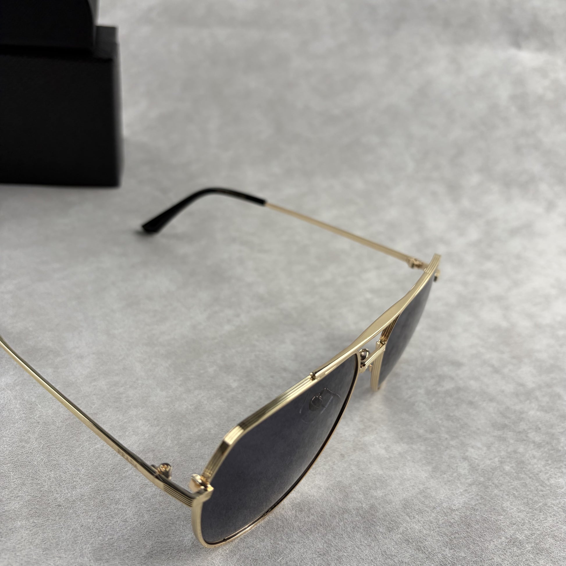 A pair of gold metal aviator sunglasses with dark lenses resting on a light grey textured background