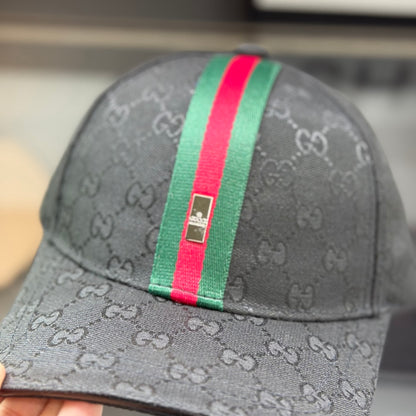 Close-up of a premium black baseball cap with a red and green center stripe and monogram pattern.