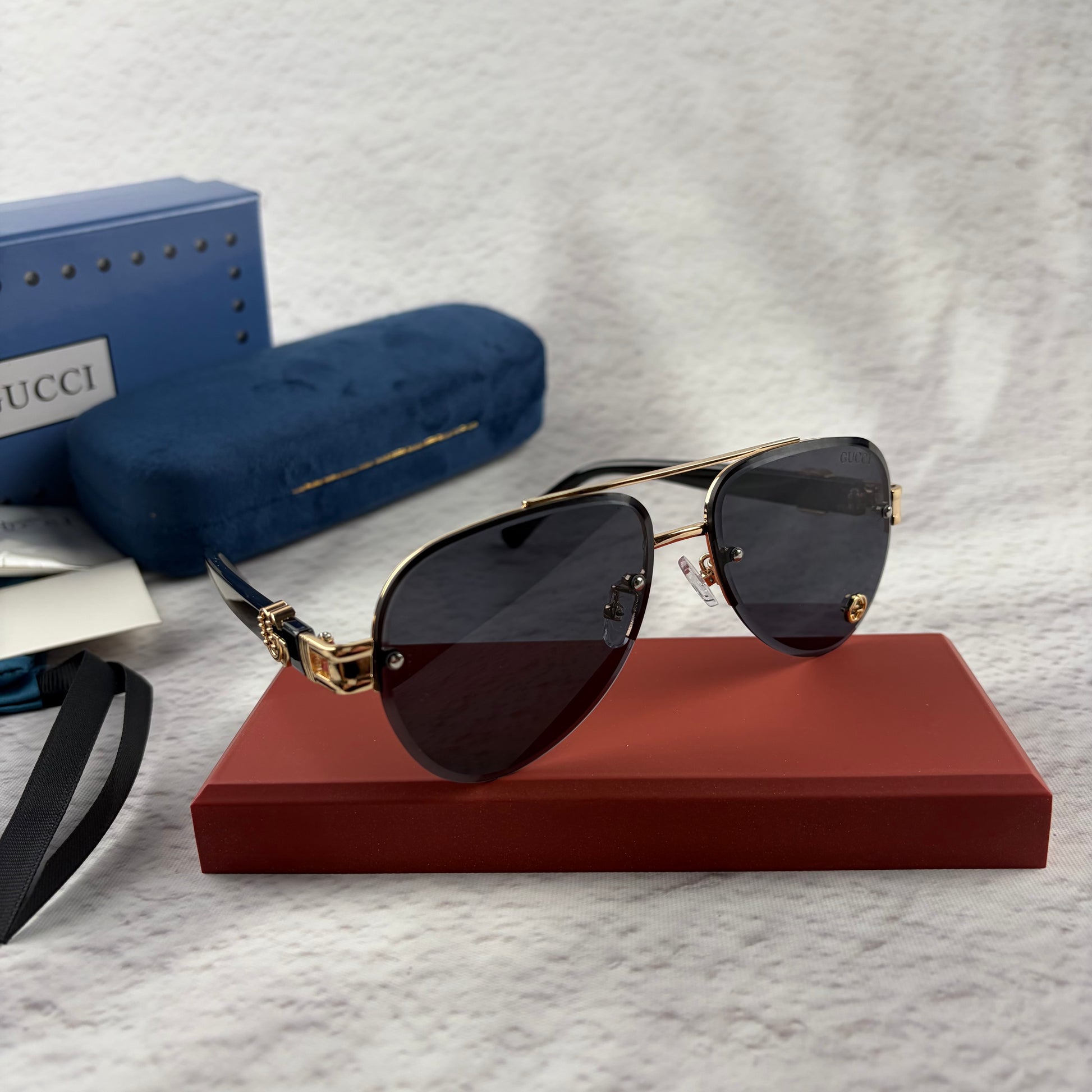 Pilot sunglasses with gold frame accents and dark lenses on a red display case.