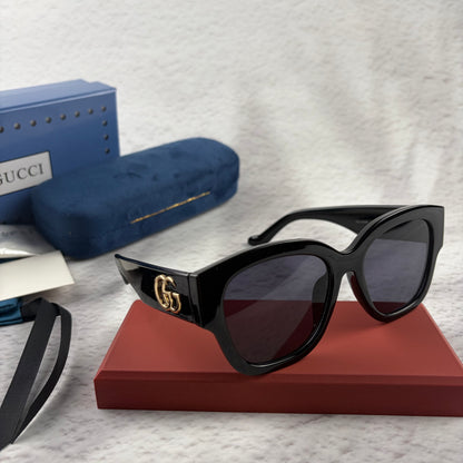 Oversized black frame sunglasses with dark gradient lenses and gold-tone logo detailing on temples.