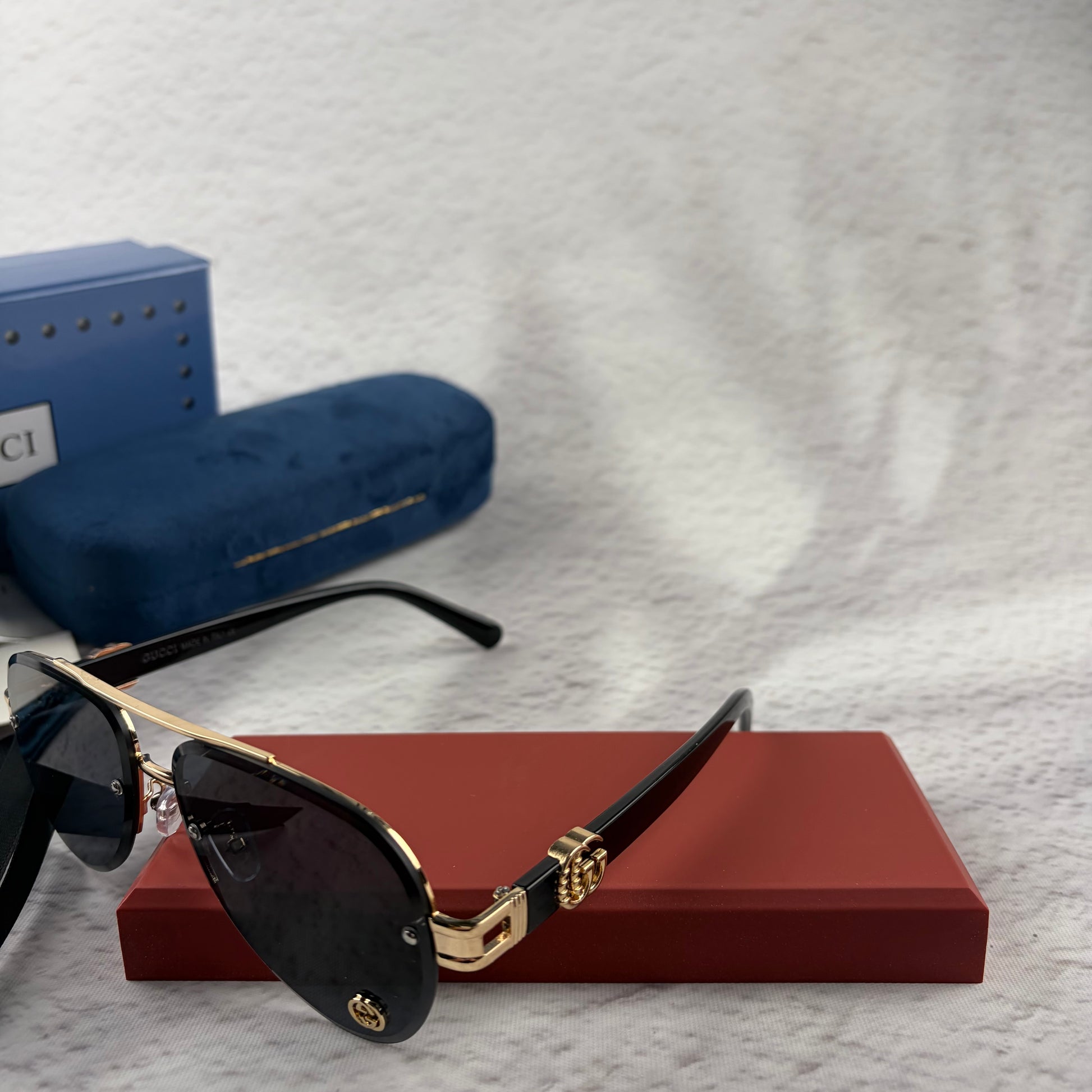 Pilot sunglasses with gold frame accents and dark lenses on a red display case.