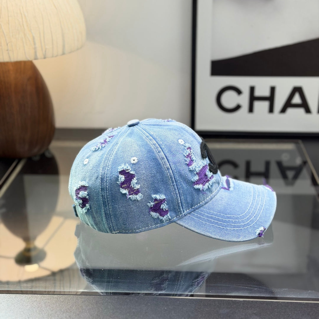 Distressed blue denim baseball cap with frayed detailing and a central stitched logo emblem.